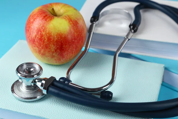 Estetoscopio médico con manzana y libros sobre fondo azul —  Fotos de Stock