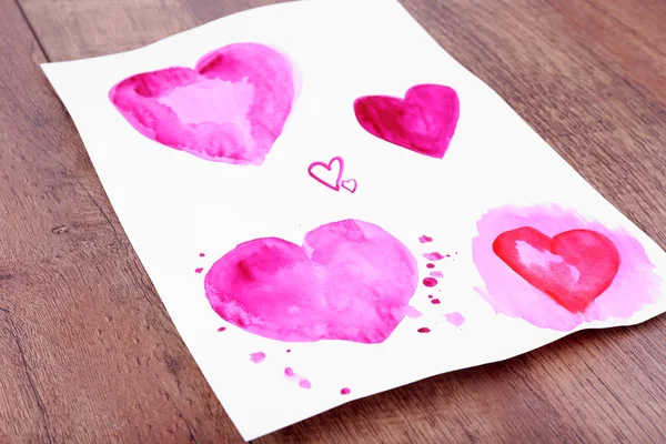 Painted hearts on sheet of paper on wooden table background — Stock Photo, Image