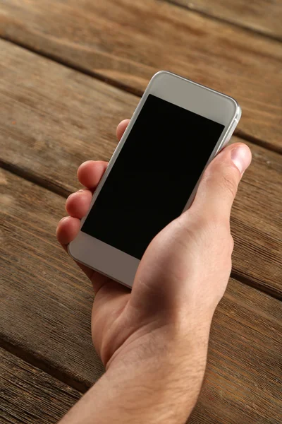 Mano sosteniendo el teléfono móvil inteligente sobre fondo de mesa de madera — Foto de Stock