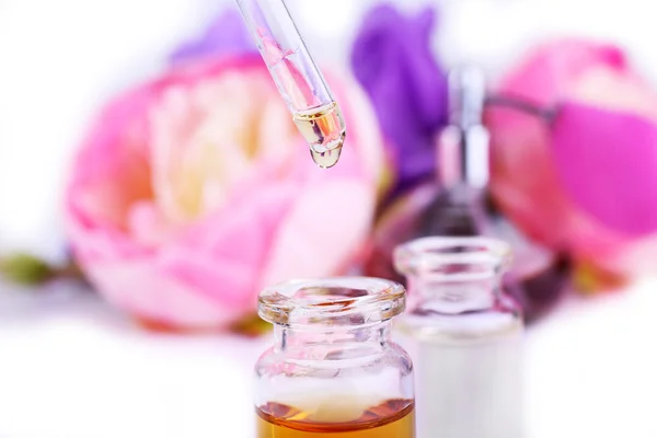 Druppelaar fles parfum met bloemen op lichte achtergrond — Stockfoto