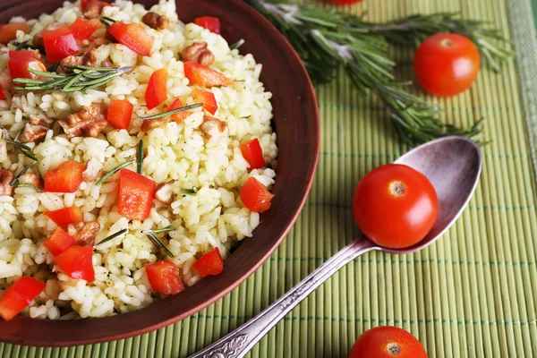 Rijst met walnoten en cherry tomaten in plaat op bamboe mat achtergrond — Stockfoto