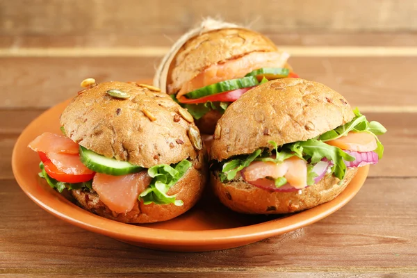 Sandwiches con salmón en plato, sobre fondo de madera — Foto de Stock