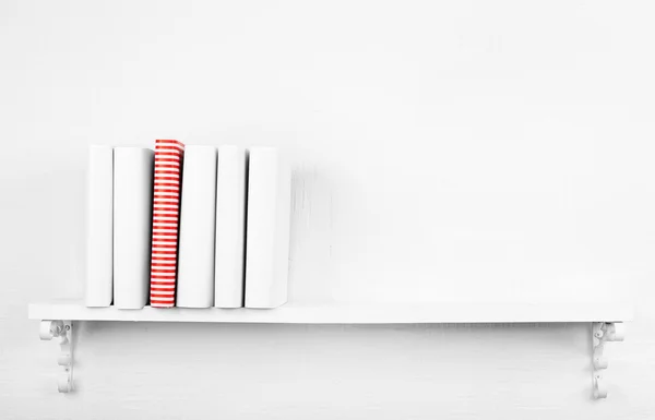 Libros en blanco con uno rojo en la estantería sobre fondo blanco de la pared — Foto de Stock