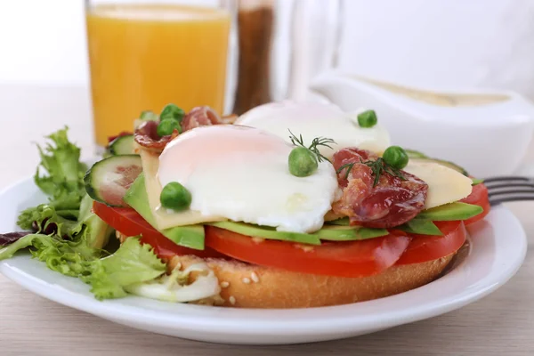 Sandwich with poached eggs, bacon and vegetables on plate on wooden background — Stock Photo, Image