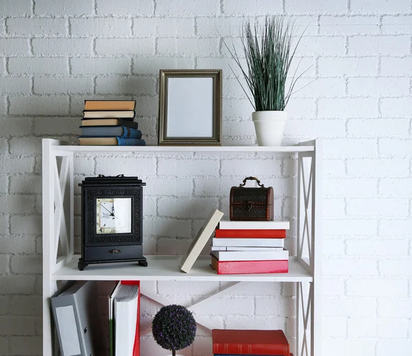 Bücherregale mit Büchern und dekorativen Objekten auf Backsteinwand Hintergrund — Stockfoto