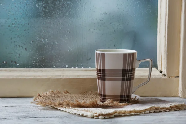 Tasse Heißgetränk mit Serviette auf Fensterbank auf Regen Hintergrund — Stockfoto