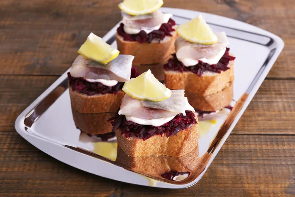 Rye toasts with herring and beets on tray on wooden background — Stock Photo, Image