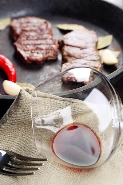 Glass of wine and steak in frying pan on table close up — Stock Photo, Image