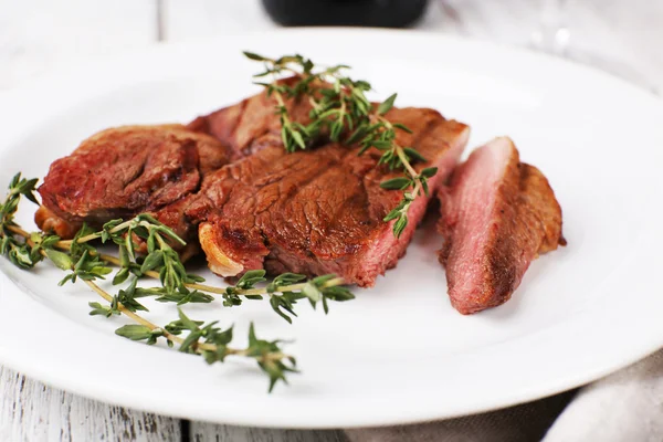 Steak with herbs on plate on wooden table — Stock Photo, Image