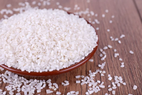 Grain of rice on plate on wooden background — Stock Photo, Image