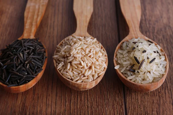 Diferentes tipos de arroz en cucharas sobre fondo de madera — Foto de Stock