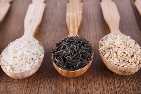 Diferentes tipos de arroz em colheres no fundo de madeira — Fotografia de Stock