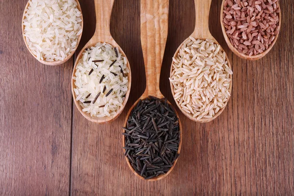 Diferentes tipos de arroz em colheres no fundo de madeira — Fotografia de Stock