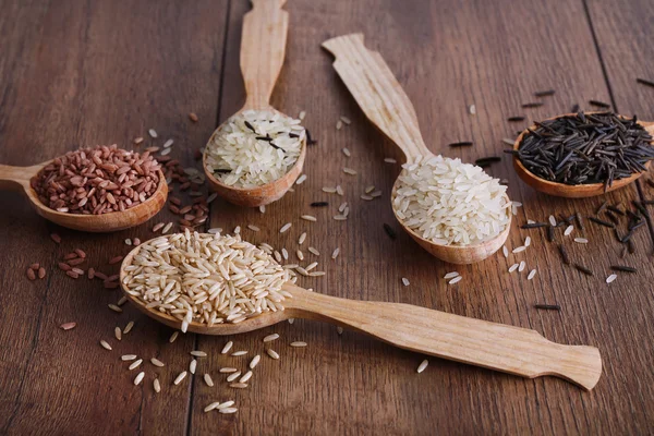 Verschiedene Reissorten in Löffeln auf hölzernem Hintergrund — Stockfoto