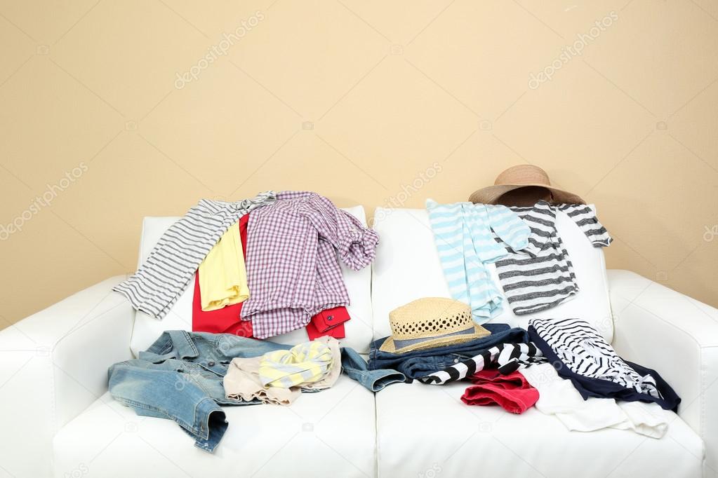 Messy clothing on white sofa, on light wall background