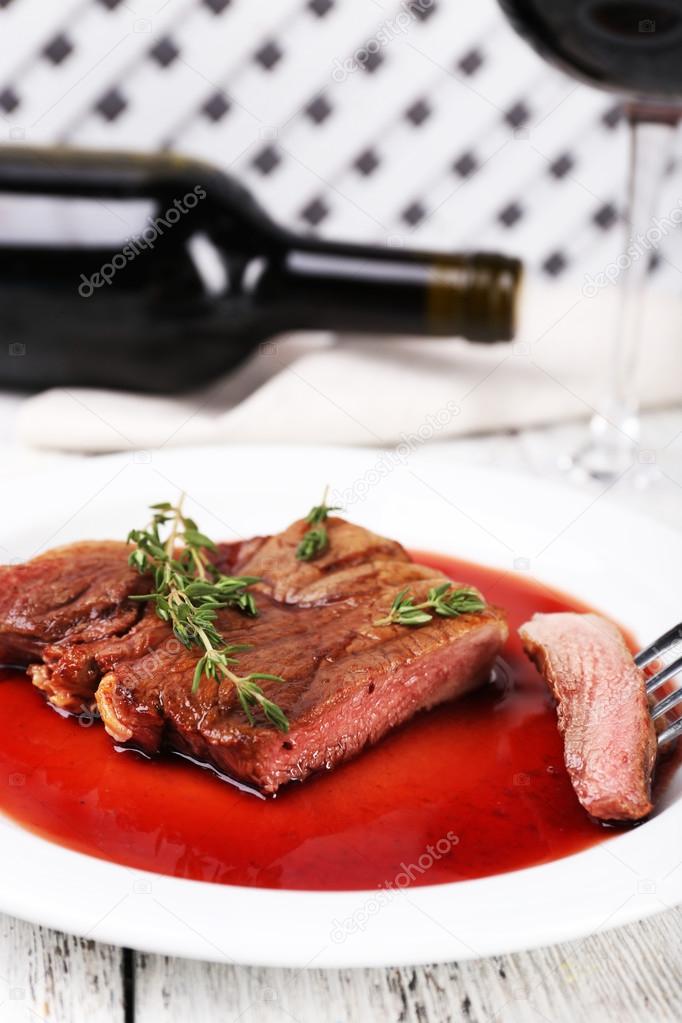 Steak with wine sauce on plate with bottle of wine on wooden background