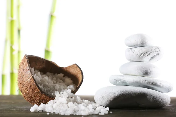 Still life of spa stones and coconut shell of sea salt on wooden surface with bamboo sticks isolated on white — Stock Photo, Image