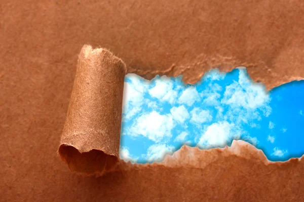 Fundo céu azul com nuvens através de papel artesanal rasgado — Fotografia de Stock