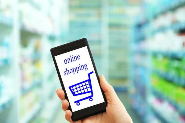 Mobile concetto di shopping. Mano che tiene il telefono cellulare per lo shopping su Internet su sfondo supermercato — Foto Stock