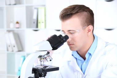 Erkek bilim adamı laboratuvarda mikroskop kullanıyor.