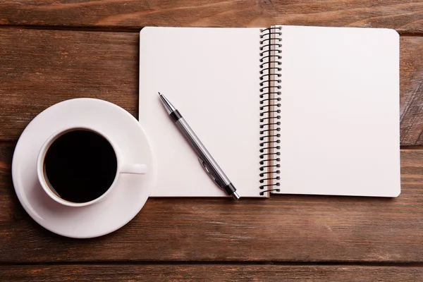 Cup of coffee on saucer with notebook and pen on wooden table background — Stock Photo, Image