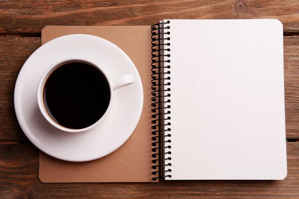 Kopje koffie op schotel met notitieblok op houten tafel achtergrond — Stockfoto