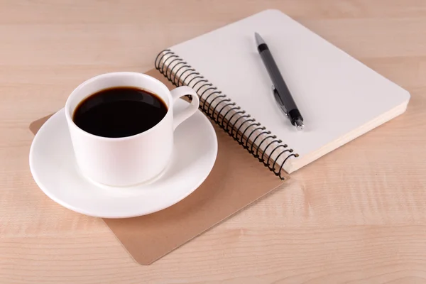 Tazza di caffè su piattino con taccuino e penna su sfondo tavolo in legno — Foto Stock