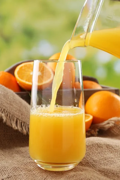 Pouring orange juice from glass carafe, on wooden table and bright background — Stock Photo, Image