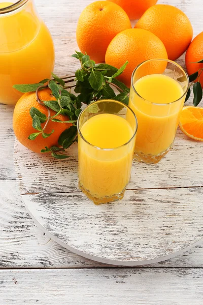 Glass of orange juice and oranges on color wooden table background — Stock Photo, Image