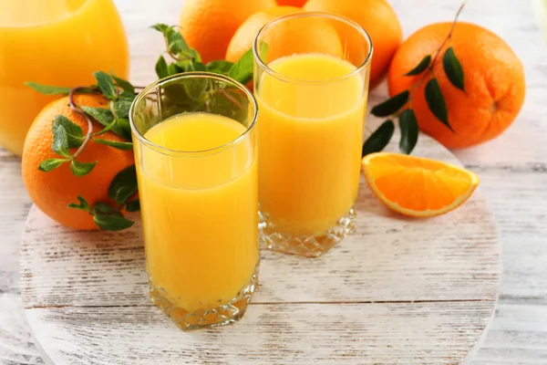 Sklenice pomerančové šťávy a pomeranče na dřevěný stůl barvy pozadí — Stock fotografie