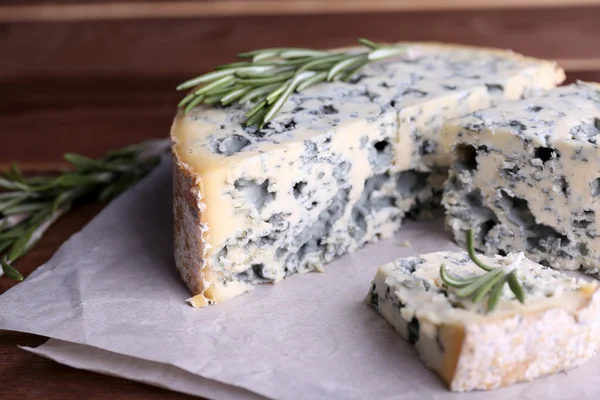 Blauwe kaas met takjes rozemarijn op vellen papier en houten tafel achtergrond — Stockfoto