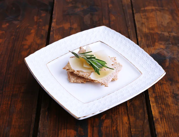 Pan crujiente con rodajas de queso parmesano con ramita de romero en plato sobre fondo de mesa de madera —  Fotos de Stock