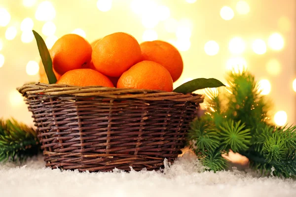 Čerstvé zralé mandarinky v proutěném koši, na sněhu, na pozadí světla — Stock fotografie