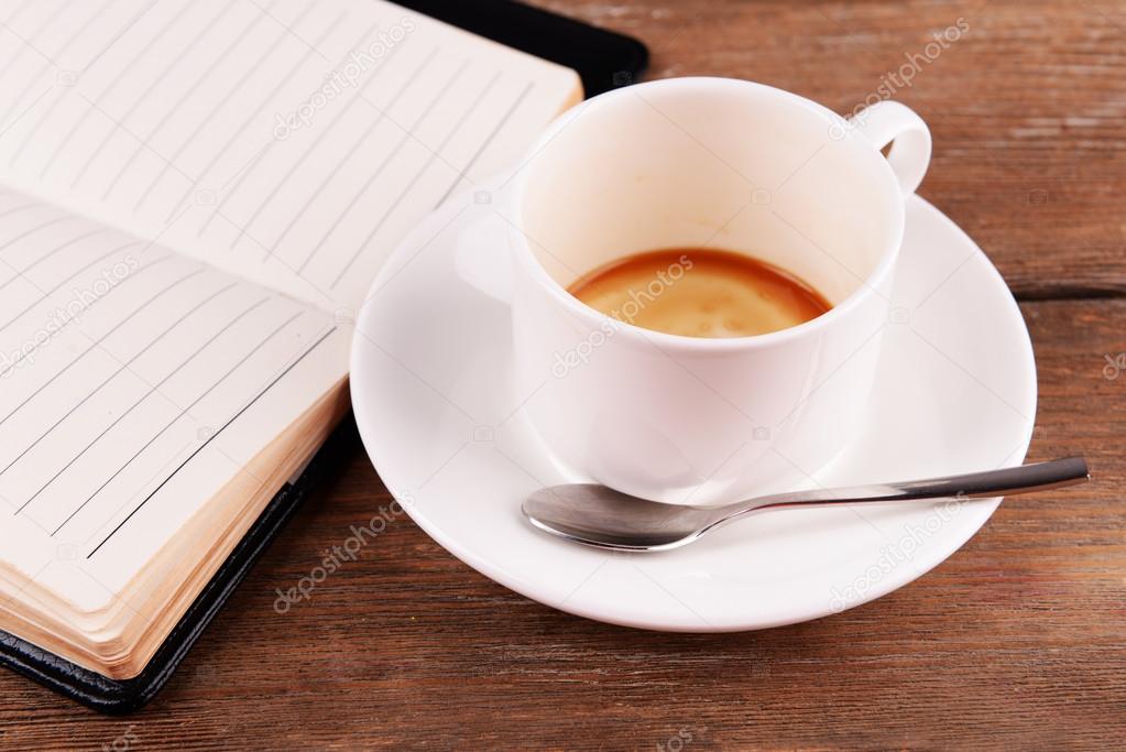 Cup of coffee on saucer with diary and spoon on wooden table background