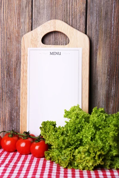 Cutting board with menu sheet of paper, with cherry tomatoes and lettuce on wooden planks background — Stock Photo, Image