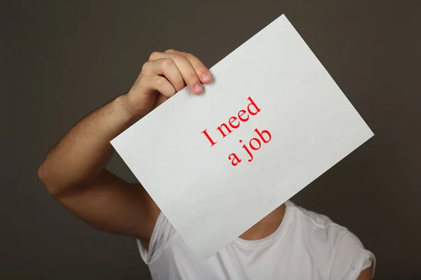 Foglio di carta con iscrizione Ho bisogno di un lavoro in mano maschile su sfondo scuro — Foto Stock