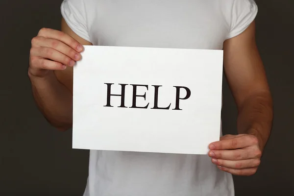 Sheet of paper with Help sign in male hands on dark background — Stock Photo, Image