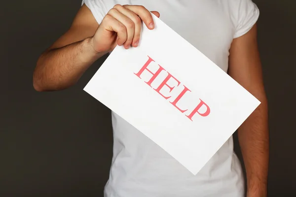 Sheet of paper with Help sign in male hand on dark background — Stock Photo, Image