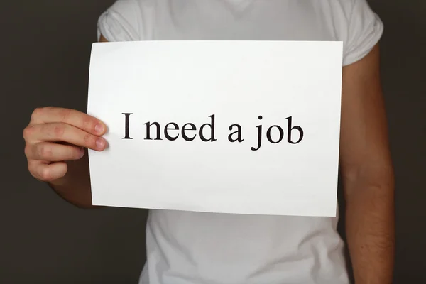 Blatt Papier mit der Aufschrift Ich brauche einen Job in Männerhand auf dunklem Hintergrund — Stockfoto