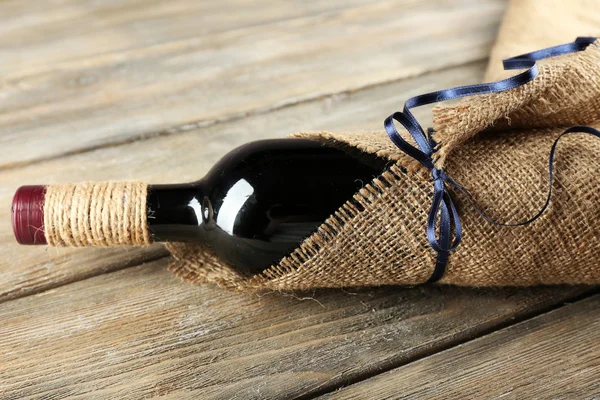 Bouteille de vin rouge enveloppée dans un tissu de toile de jute sur des planches en bois — Photo