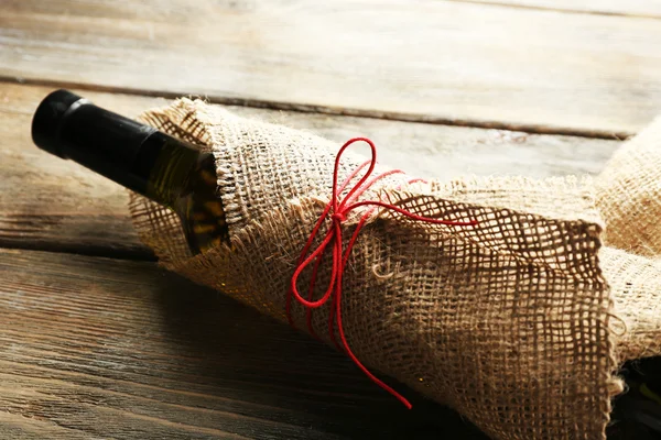 Bouteille de vin enveloppée dans un tissu de toile de jute sur des planches en bois — Photo