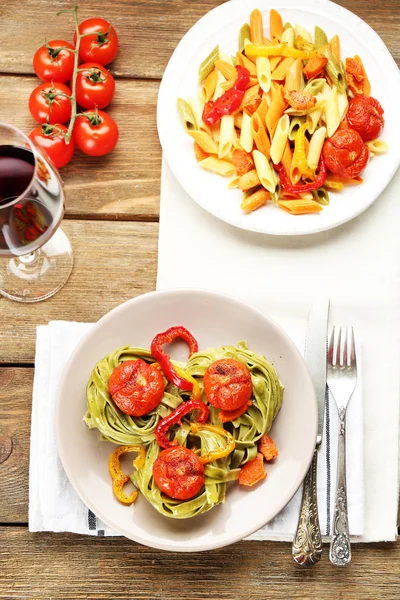 Zwei Arten von leckeren Nudeln mit Paprika, Karotten und Tomaten auf Holztischhintergrund — Stockfoto