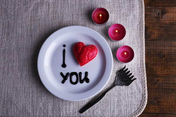 Cookie in vorm van hart op plaat met opschrift ik hou van jou, en kaarsen op servet en houten tafel achtergrond — Stockfoto