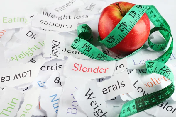 Papers with different words, apple and measuring tape close up — Stock Photo, Image