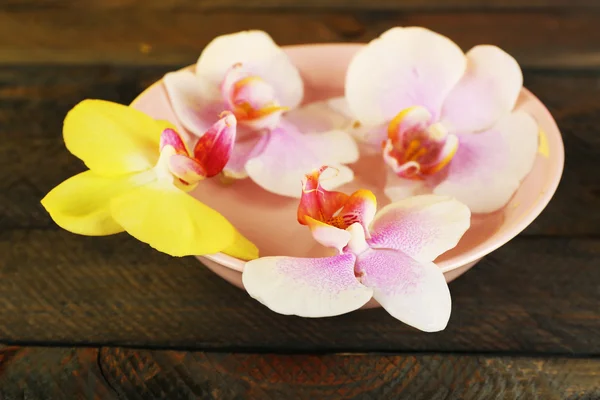 Ciotola con orchidee su fondo di legno — Foto Stock