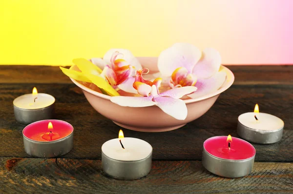 Ciotola con orchidee e candele sul tavolo su sfondo luminoso — Foto Stock