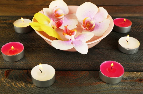 Cuenco con orquídeas y velas sobre fondo de madera — Foto de Stock