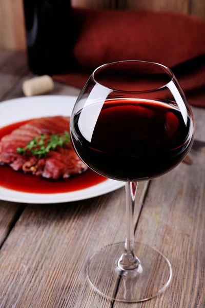 Glass of wine with grilled steak in wine sauce on wooden background — Stock Photo, Image