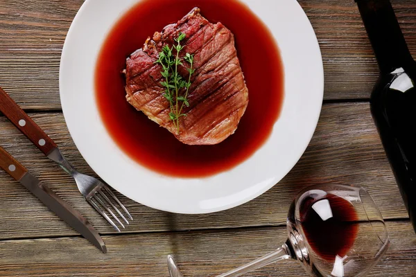 Grilled steak in wine sauce with bottle of wine on wooden background — Stock Photo, Image