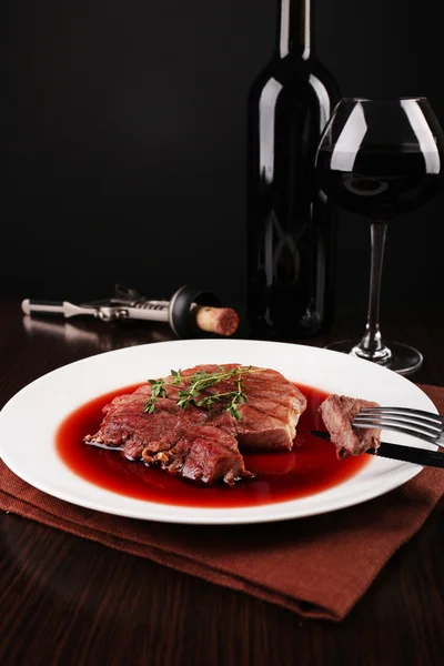 Bife grelhado em molho de vinho com copo de vinho no fundo escuro — Fotografia de Stock